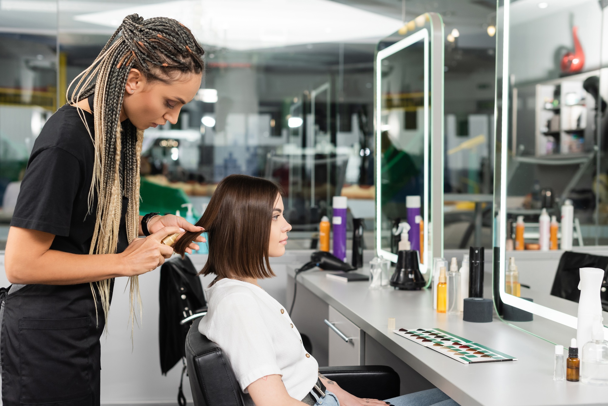 beauty salon work, professional salon worker with braids applying oil on hair of female client,